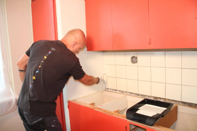 Muž maluje dlažbu v kuchyni při rekonstrukci linky.