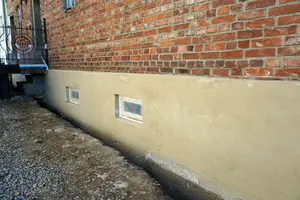 Venkovní vápenná omítka na zdivu domu s malými okny.