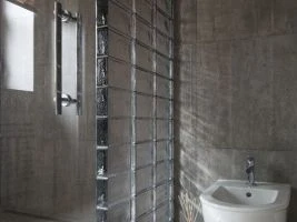 Moderní koupelna s šedými dlaždicemi, umyvadlem a skleněnou přepážkou.