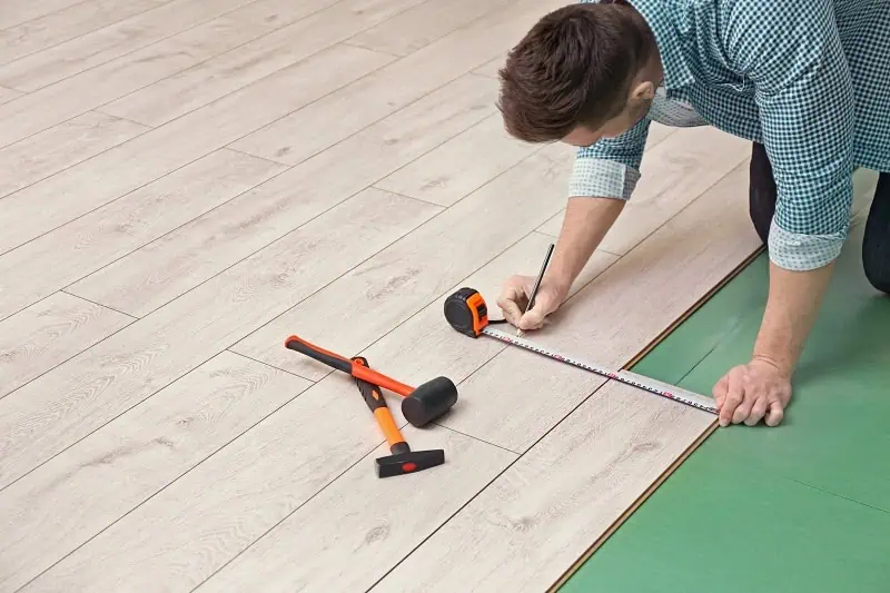 Muž měří podlahové desky při instalaci laminátu nebo vinylové podlahy.