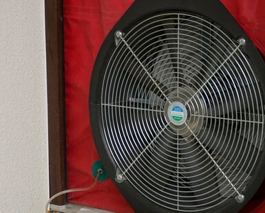 Průmyslový ventilátor s červeným krytem na zdi.