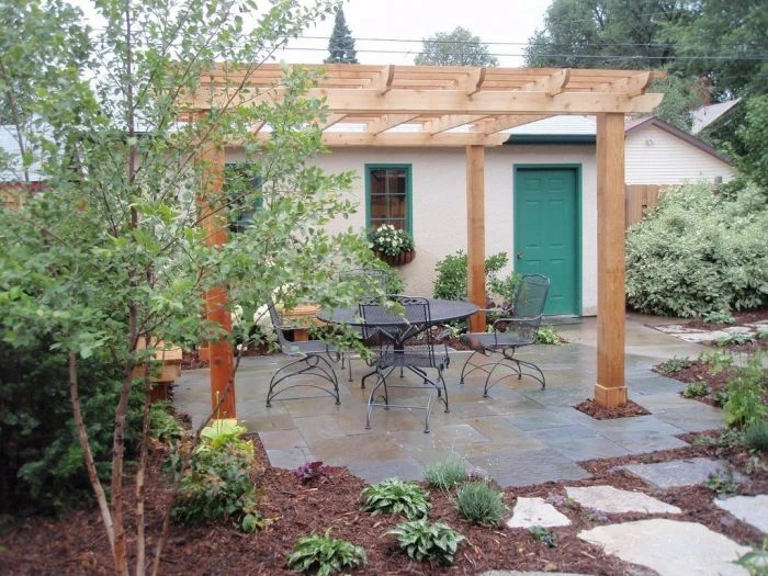 Dokončená dřevěná pergola nad terasou s nábytkem v zahradním prostředí.