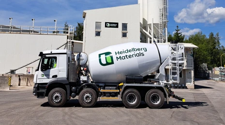 Bílý betonový smíchávač značky Heidelberg Materials před továrnou.