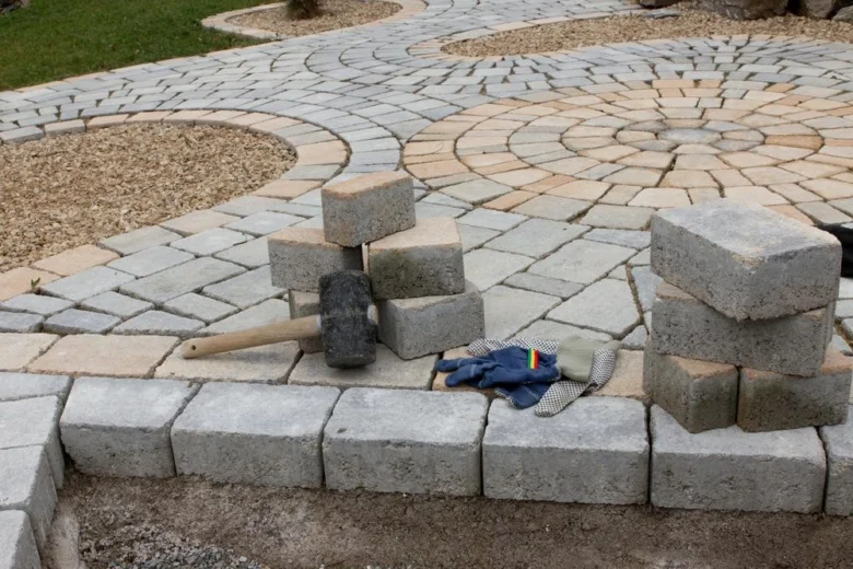 Sedí betonová dlažba s kladivem rukavicemi pro instalaci.