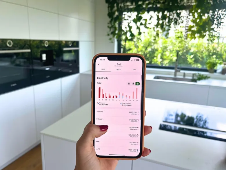 Smartfon s aplikací pro sledování spotřeby elektřiny v kuchyni.