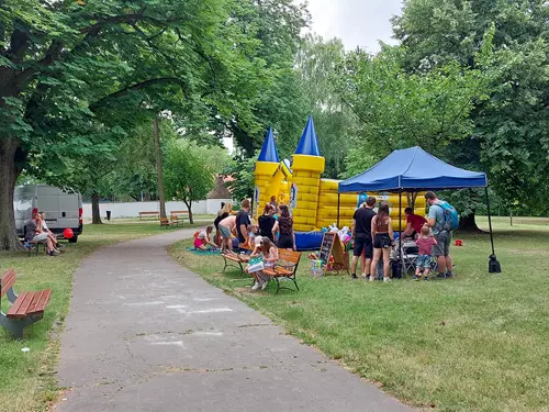 Skákací hrad na trávníku v parku s lidmi u koupaliště.