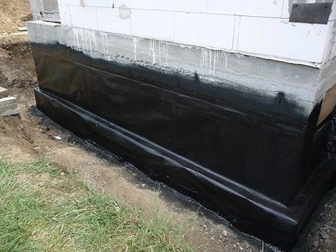 Černá hydroizolace je nanášena na betonovou základovou stěnu.