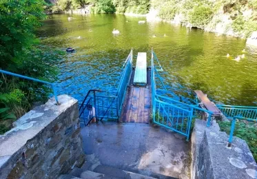 Koupaliště s modrými schody vedoucími do vody v přírodním prostředí.
