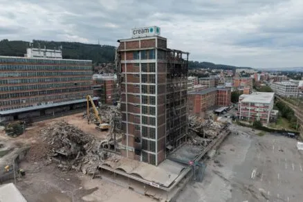 Stavební areál s demolovanou budovou a těžkou technikou.