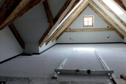 Neúpravený strop s dřevěnými trámy v podkroví během rekonstrukce.