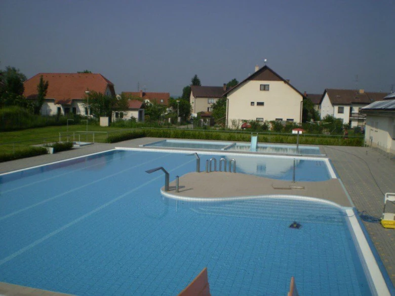 Venkovní plavecký bazén v obci Blatná s okolními domy.