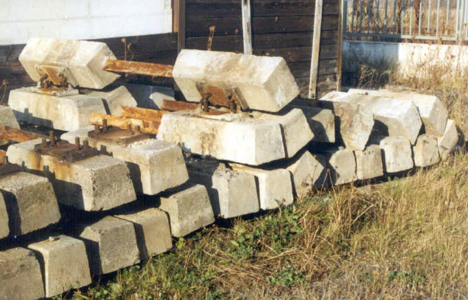 Náklad starých betonových pražců s kovy na trávníku.