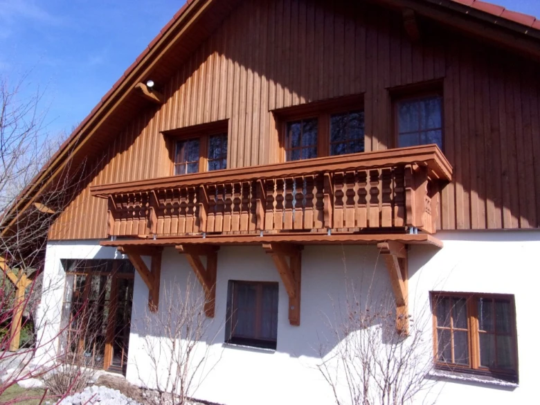 Dřevěné zábradlí na balkóně domu s bílou fasádou.