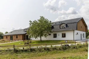 Přestavba stodoly na moderní dům s bílou fasádou a šedou střechou.