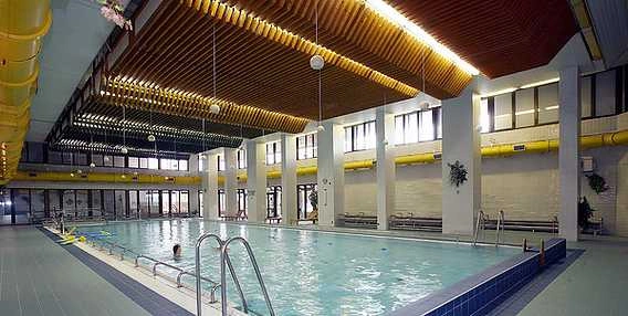 Vnitřní plavecký bazén s dřevěným stropem a žlutými ventilačními potrubími.