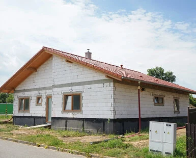 Bílá izolovaná fasáda domu při zateplování s červenou střechou.