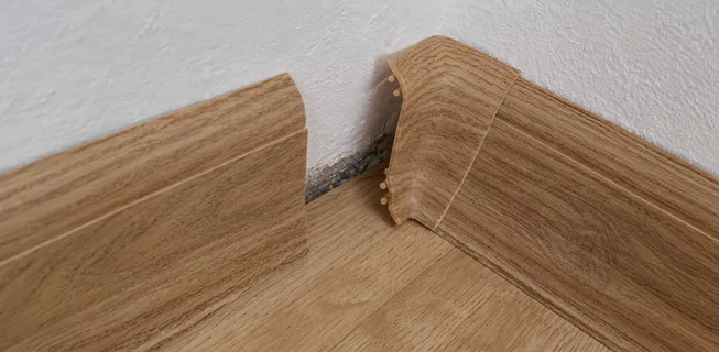Poškozený roh vinylové podlahy u zdi s prasklinami.
