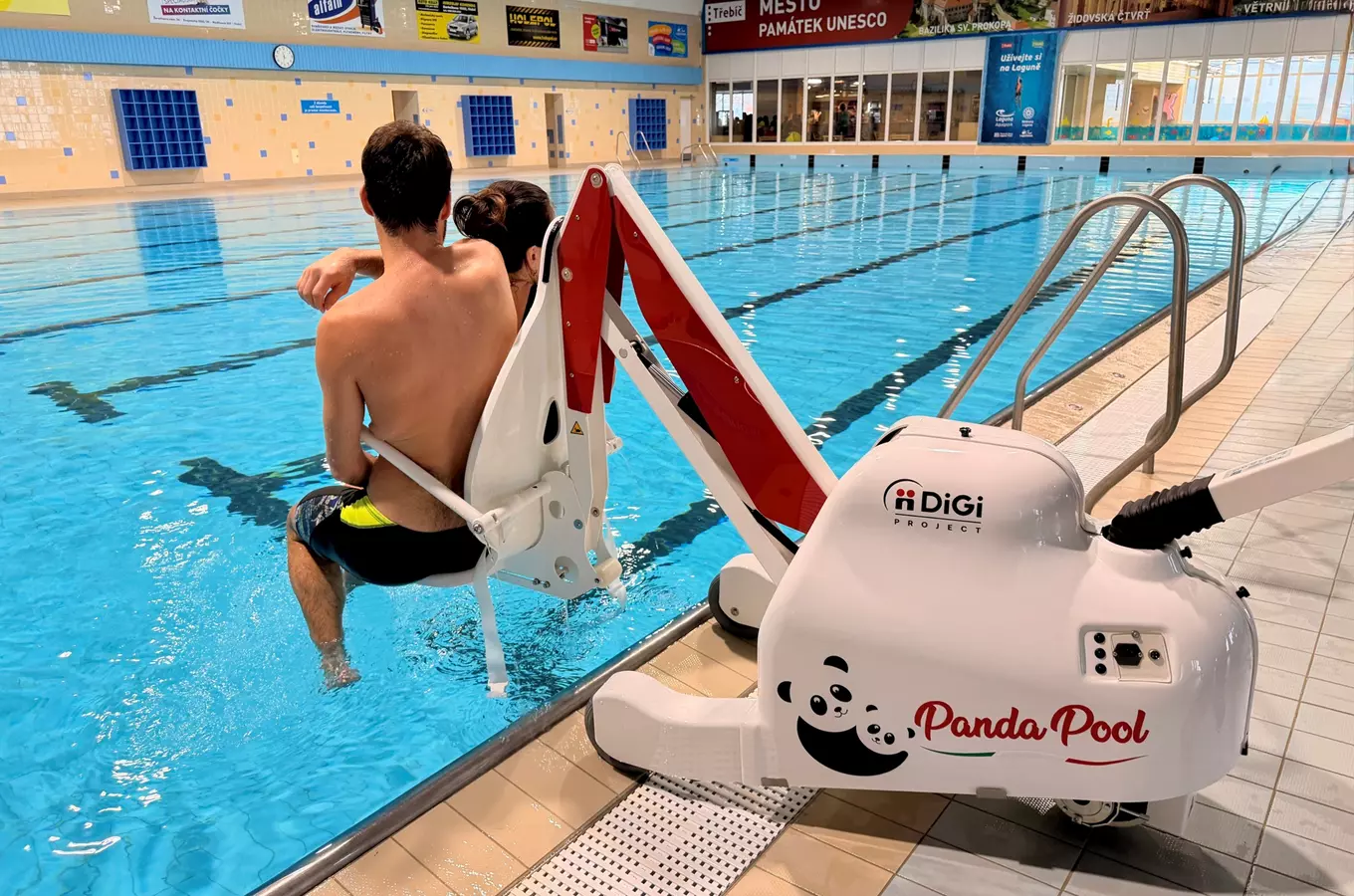 Muž a žena vstupují do bazénu pomocí vodního invalidního vozíku Panda Pool.
