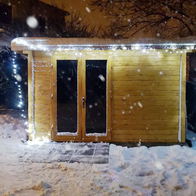 Dřevěná zahradní bouda s okny v zimním sněhu.