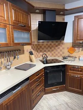 Moderní kuchyň s dřevěnými skříněmi a bílými pracovní deskami.