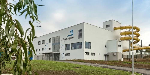 Bílá budova aquaparku s žlutou vodní skluzavkou venku.