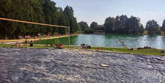 Koupaliště v Jeseníkách s bazénem, stromy a volejbalovou síť.