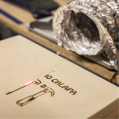 Laser gravíruje nápis na dřevě s viditelnými nástroji.
