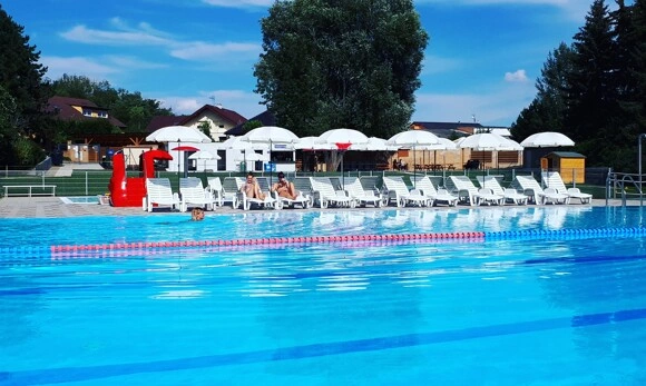 Venkovní bazén s lehátky pod slunečníky na českém letním koupališti.