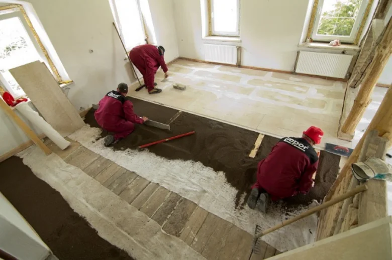 Práce na betonové podlaze s rozkládáním lepidla pro dlažbu.