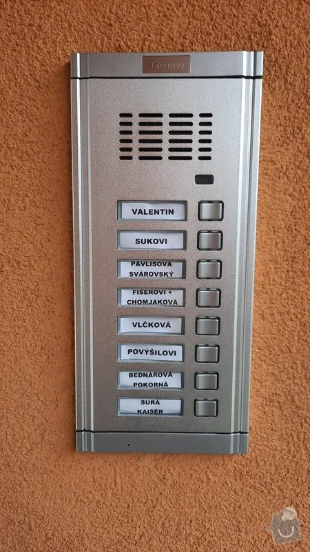 Stříbrný domovní zvonkový systém s tlačítky pro jednotlivé byty.