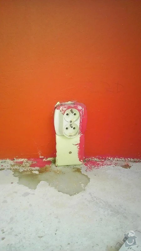 Poškozená elektrická zásuvka na zdi s odlupující se barvou.