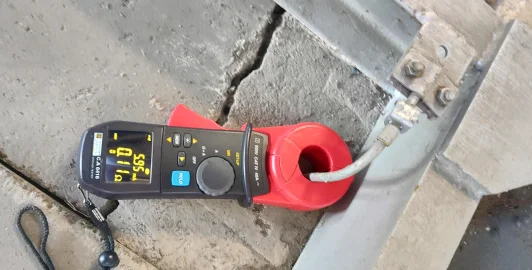 Červený ampérmetr s kleští na elektrickém kabelu v betonovém potrubí.