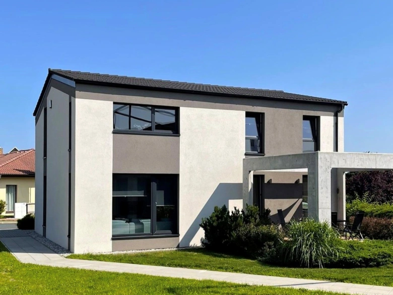 Moderní betonový dům s terasou na pozadí zelené trávy.