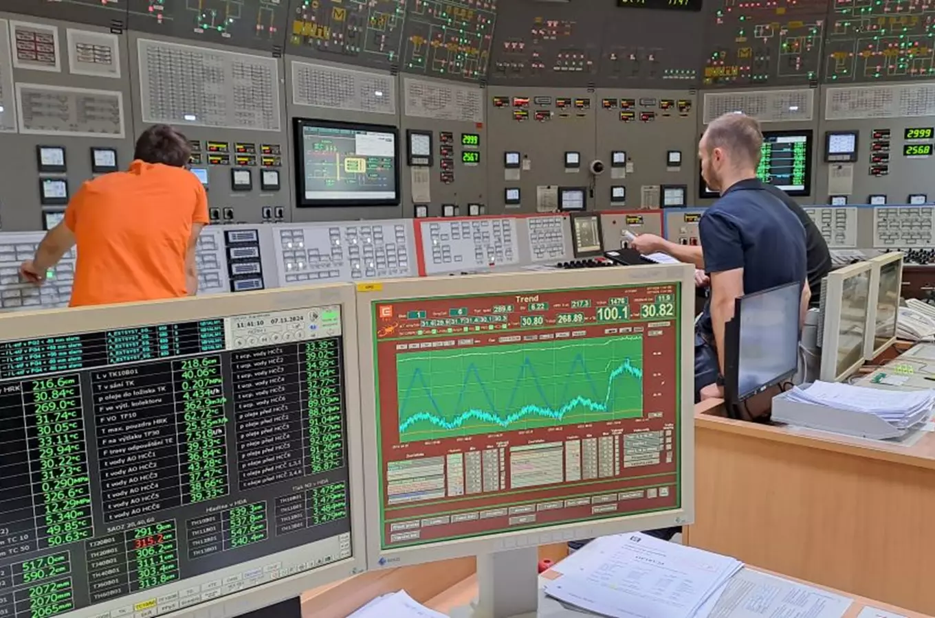 Ovládací místnost jaderné elektrárny s operátory a monitorovacími systémy.