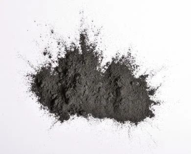 Hromada tmavě šedého prachu grafitu na bílém pozadí.