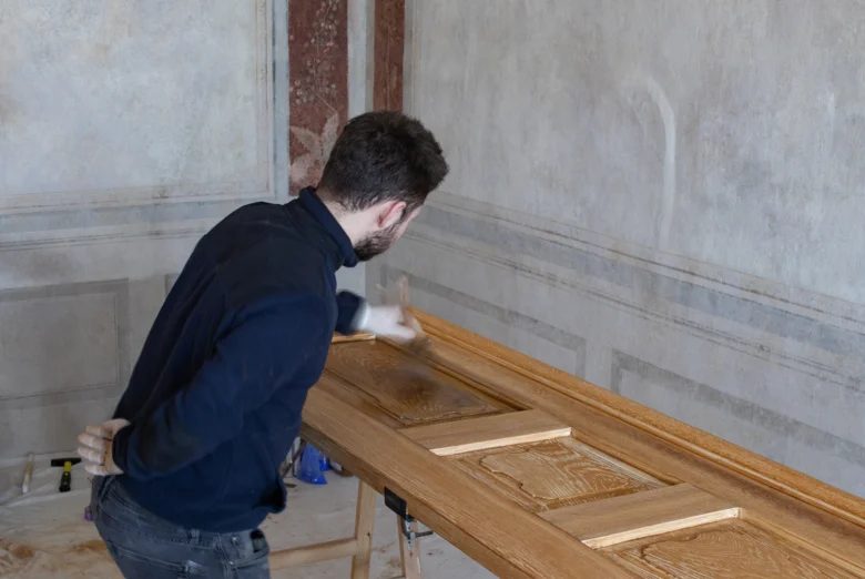 Muž aplikuje dřevěný flád na dveře pomocí malého nástroje.