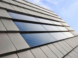 Fotovoltaické panely na střeše budovy pod modrou oblohou.