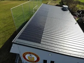 Fotovoltaické panely na střeše budovy vedle trávníku.
