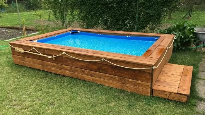 Obdélníkový bazén s dřevěným obkladem na trávníku.
