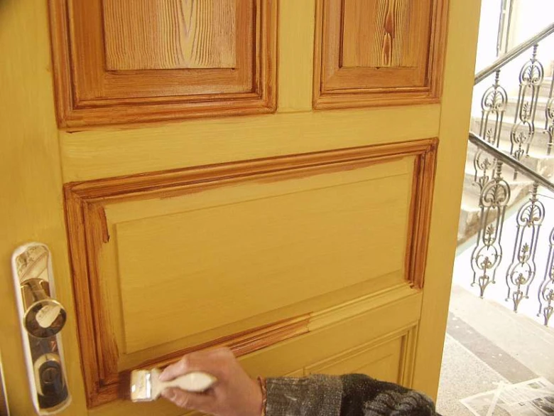Ruční aplikace žluté barvy na poškozenou dřevěnou dveřní desku.