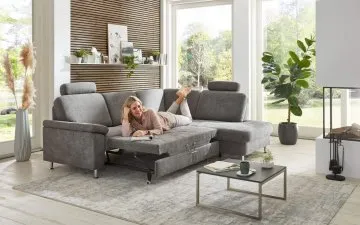 Žena odpočívá na šedé rozkládací sedací soupravě v obývacím pokoji.