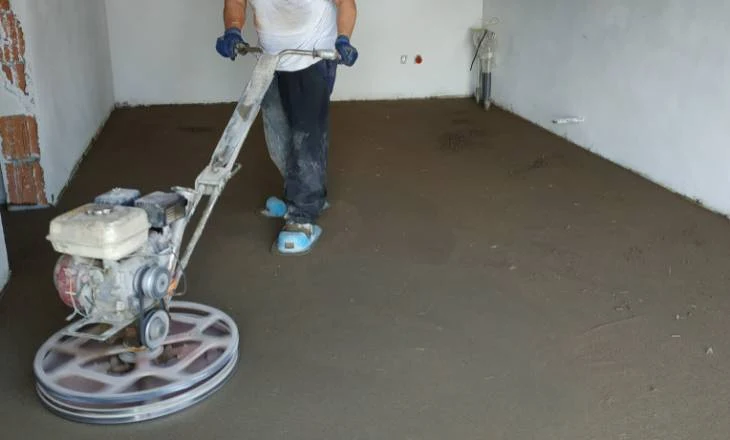 Muž leští betonovou podlahu pomocí strojního brusky.