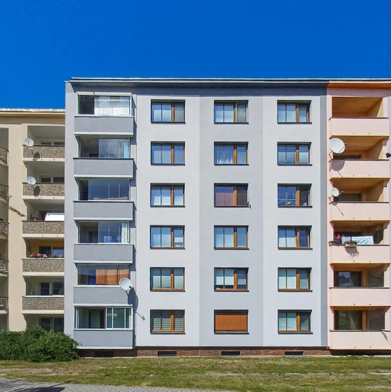 Renovovaná fasáda bytového domu s novými okny na modré obloze.