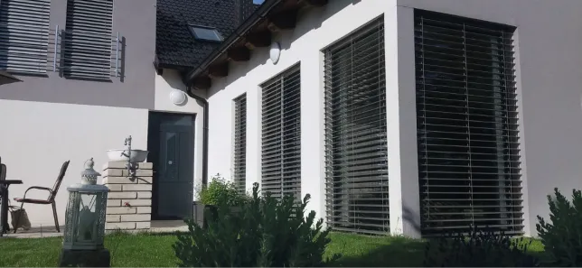 Venkovní žaluzie na oknech bílého domu v zahradě.